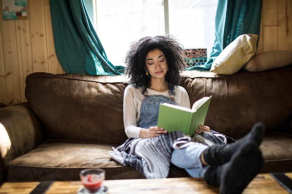 African-american-woman-reading-book-on-her-couch-imposter-syndrome-books