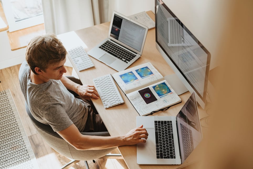 Man-in-pajamas-working-from-home-with-3-monitors-and-laptop-unique-employee-benefits