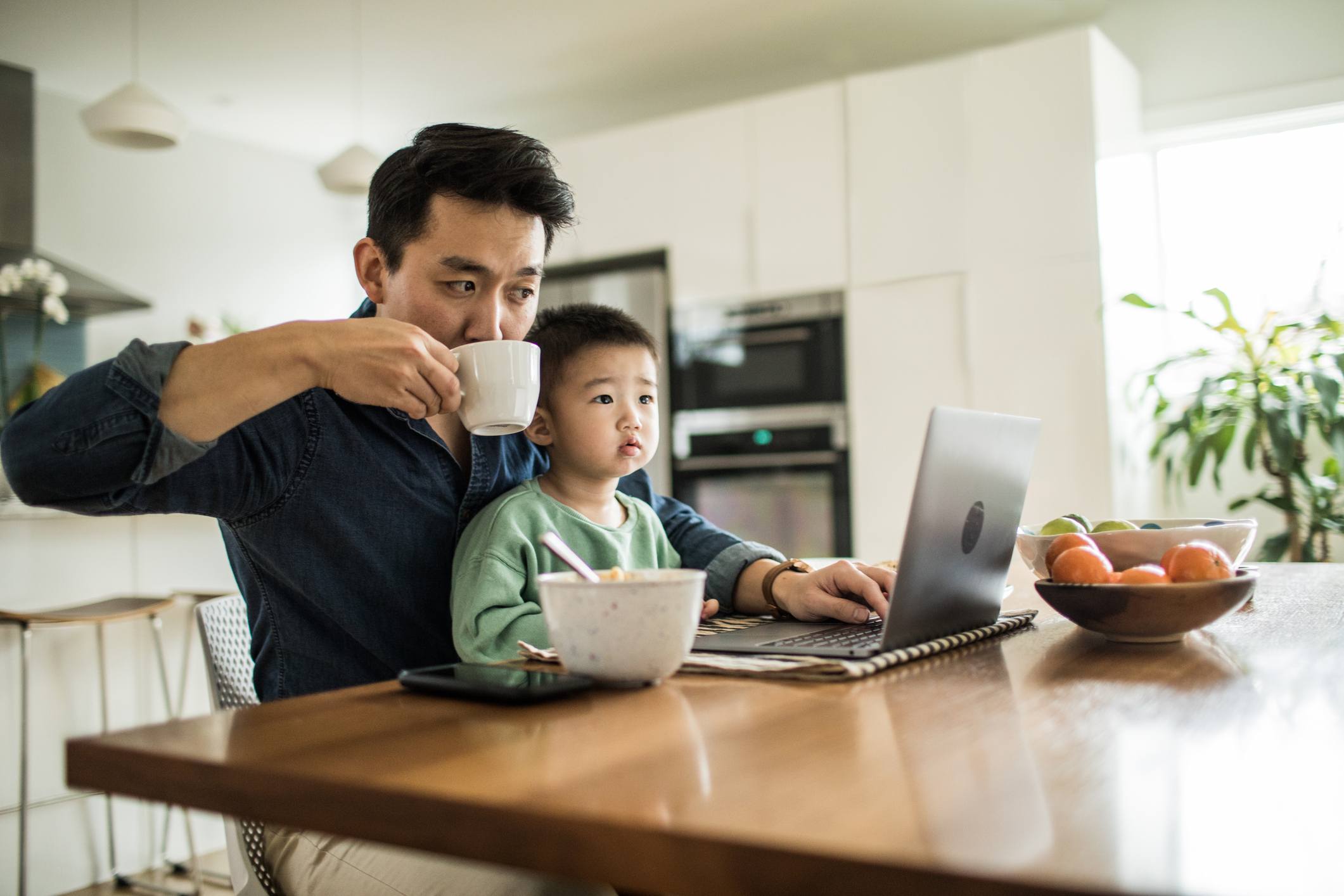 Man-with-his-toddler-son-at-his-kitchen-working-from-home-absenteeism