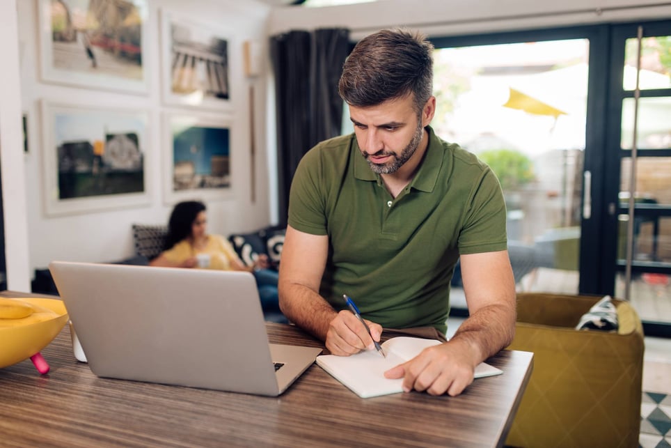 Middle-age-man-at-home-looking-at-laptop-and-writing-on-notebook-how-far-back-should-a-resume-go