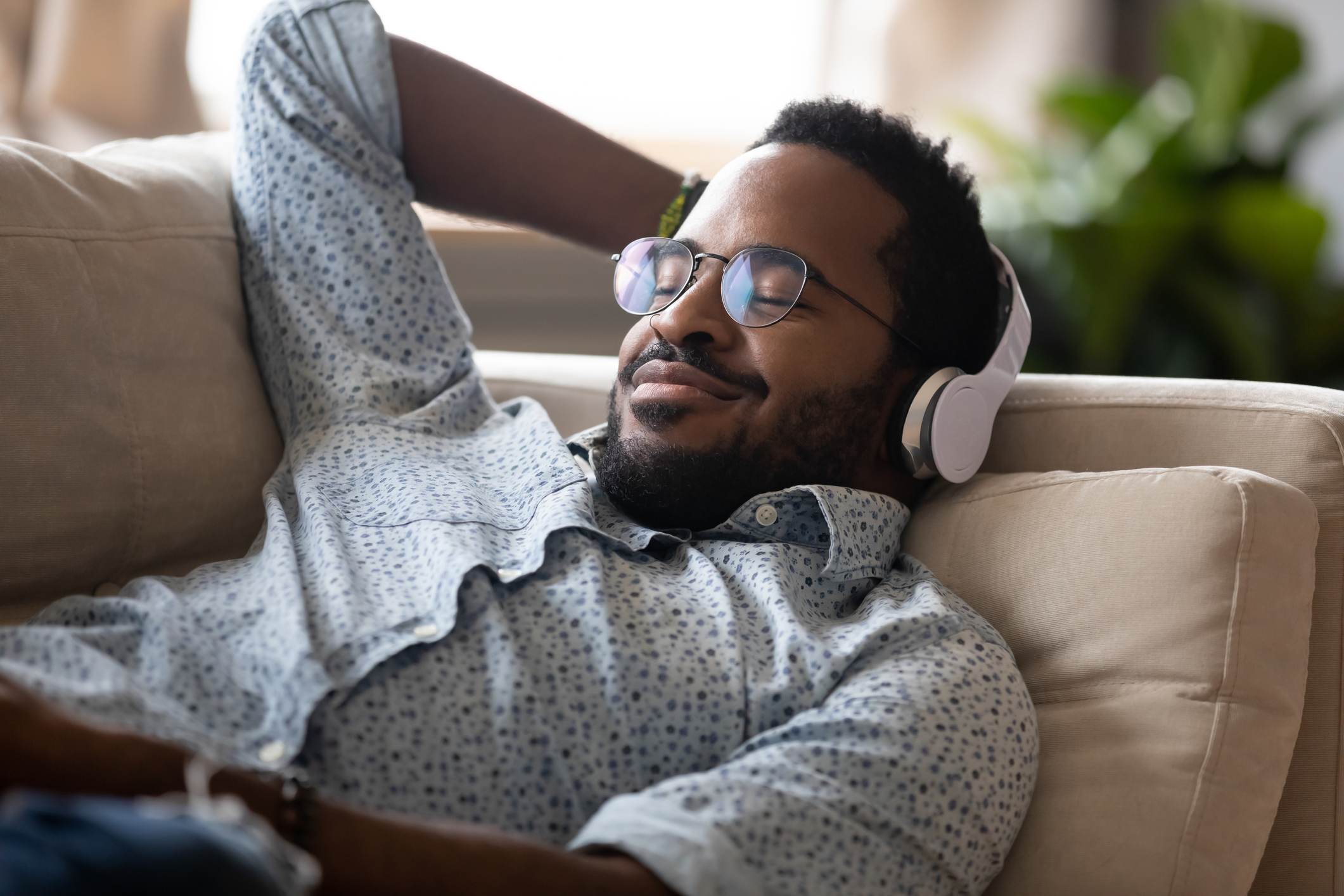 Serene-african-man-lying-on-sofa-music-relaxation-for-stress