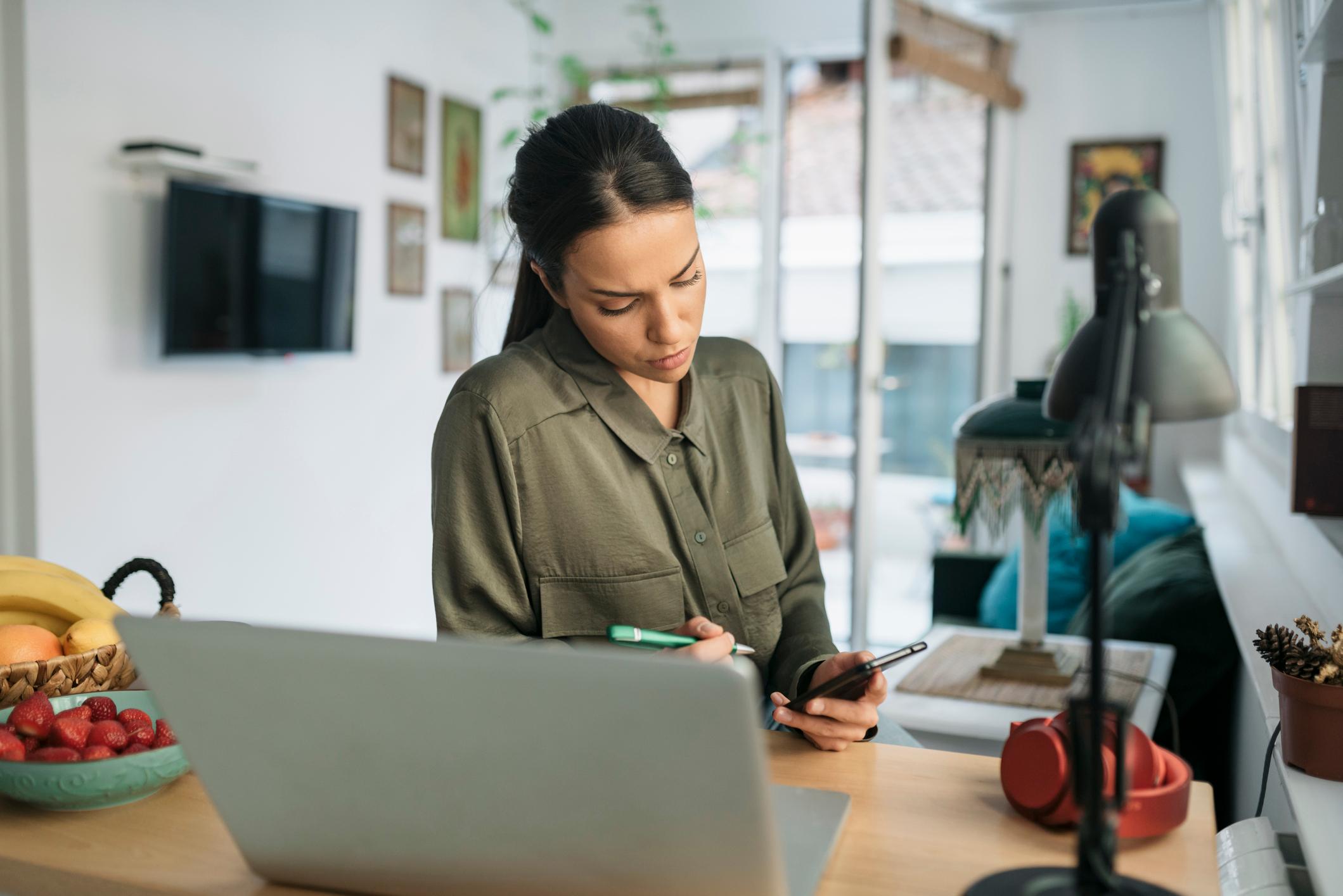 Thoughtful-woman-at-home-with-pencil-looking-at-laptop-and-phone-how-far-back-should-a-resume-go