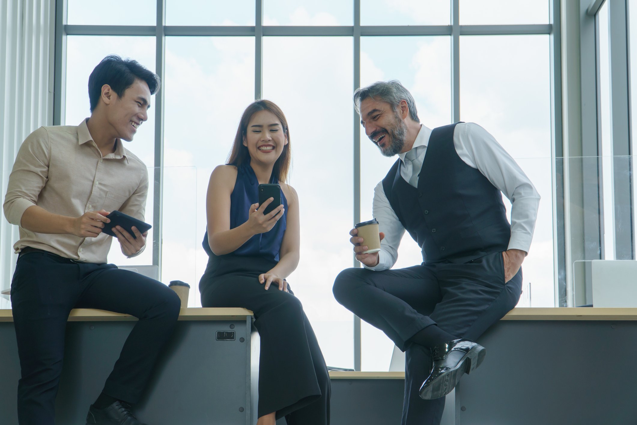 Three-coworkers-looking-at-phone-and-laughing-at-their-break-workplace-environments