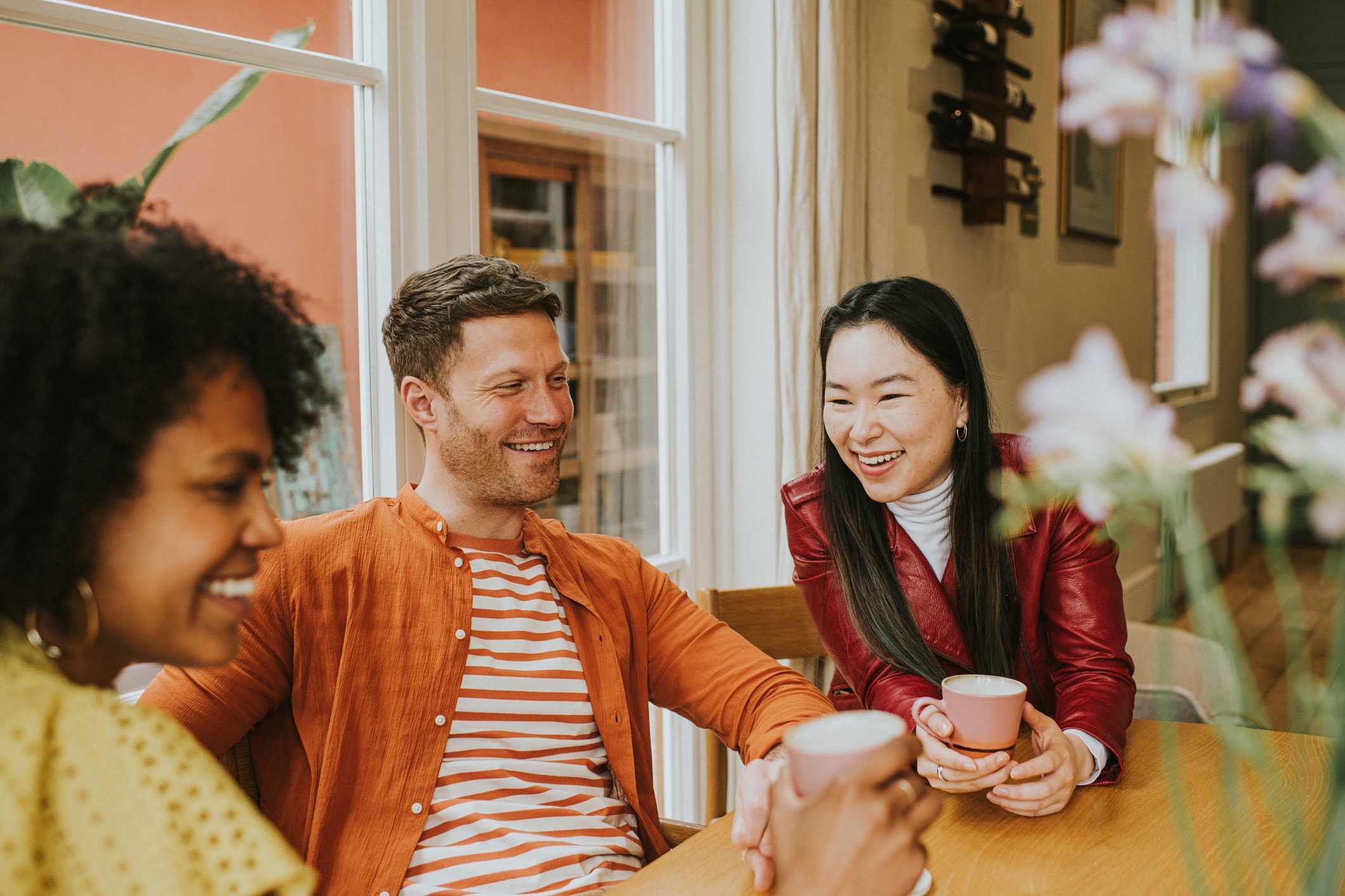 Three-young-people-sit-around-a-table-and-giggle-as-they-have-a-lighthearted-discussion-and-drink-coffee-purpose-of-anger-emotion