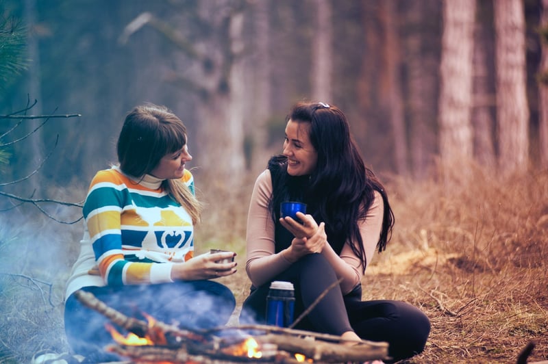 Two-women-deep-talking-at-bonfire-with-coffee-in-the-woods-deep-questions-to-ask