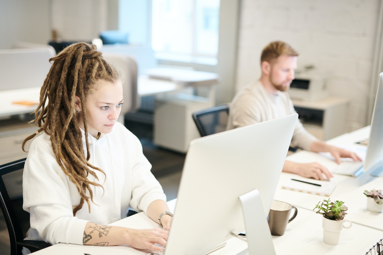 Woman-at-her-office-writing-on-computer-beside-coworker-how-to-send-a-reminder-email