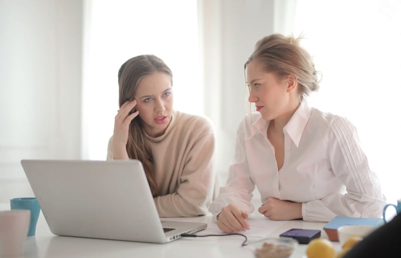 Woman-talkign-to-her-friend-while-working-together-on-laptop-how-to-message-a-recruiter-on-LinkedIn