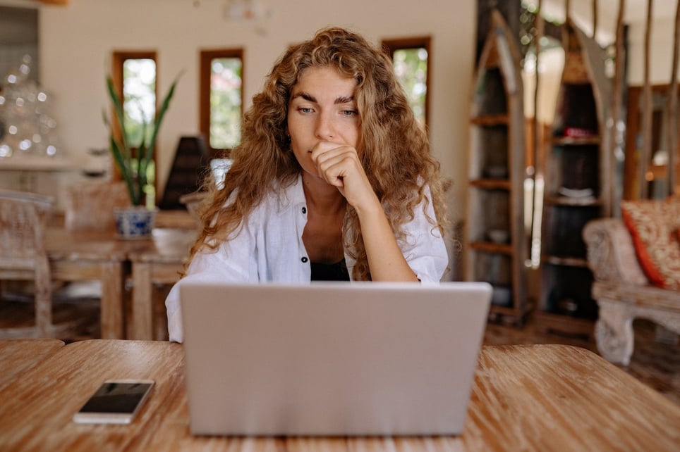 Woman-thinking-while-looking-at-laptop-at-coffee-shop-how-to-send-a-reminder-email