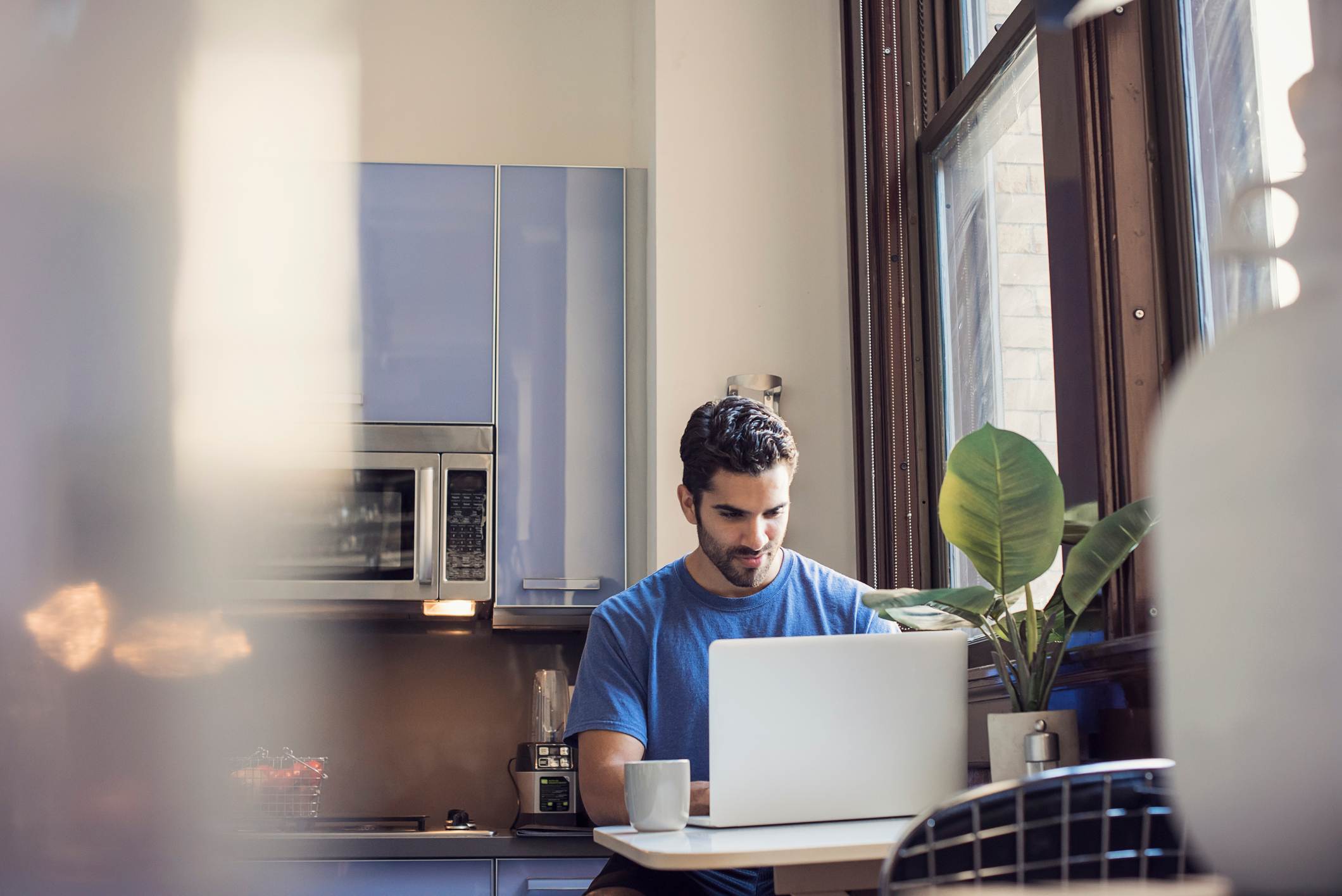 Young-man-standing-in-kitchen-using-laptop-goodbye-email-to-coworkers
