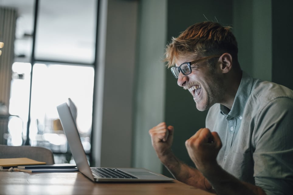 Young-man-using-laptop-laughing-happly-how-to-set-daily-goals