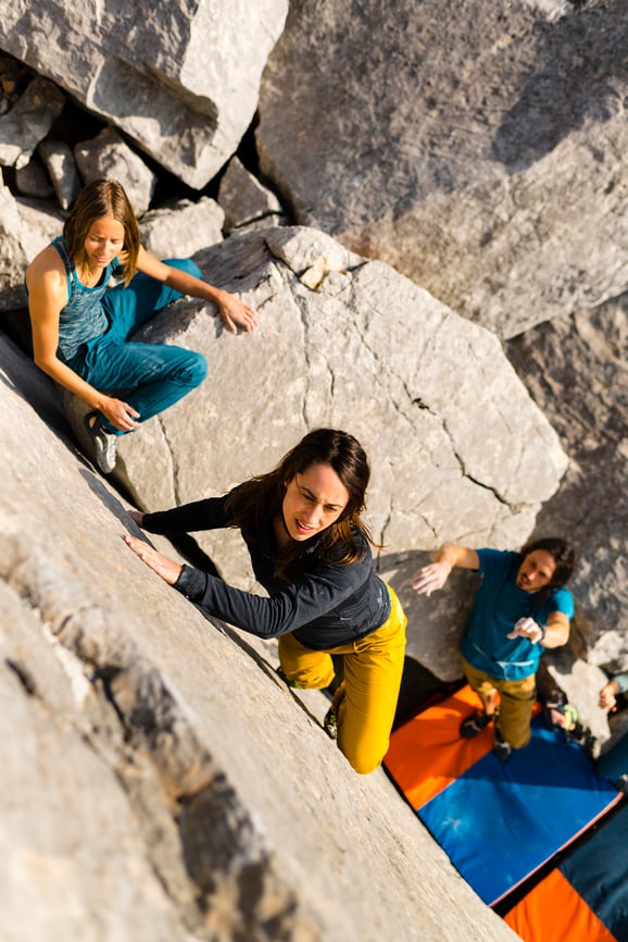 woman-climing-rock-with-2-others-supporting-from-below-empowerment-at-work